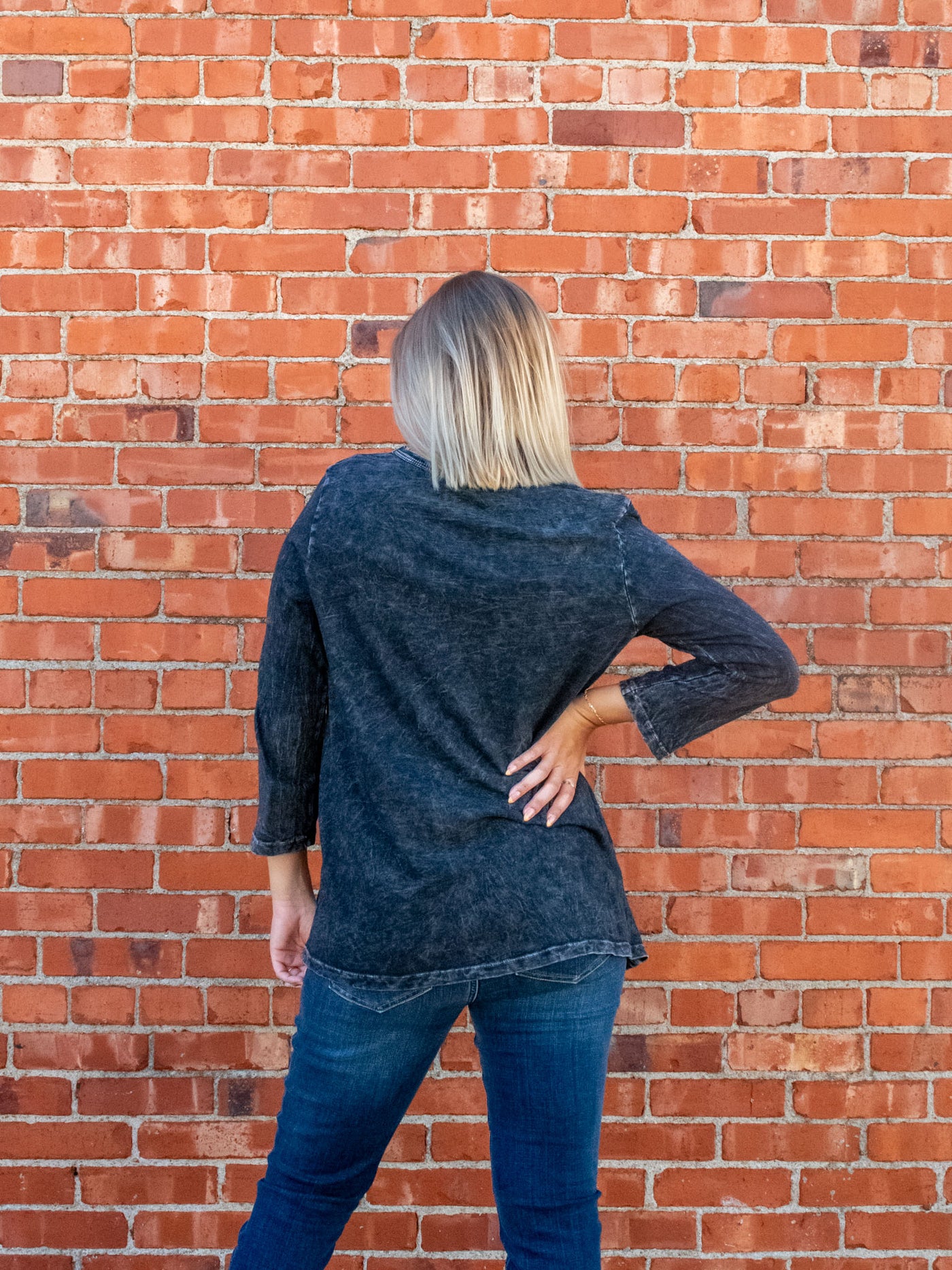 A model wearing a gray, mineral washed, 3/4 sleeve length top with a sunflower graphic. The model has it paired with a pair of medium washed skinny jeans.
