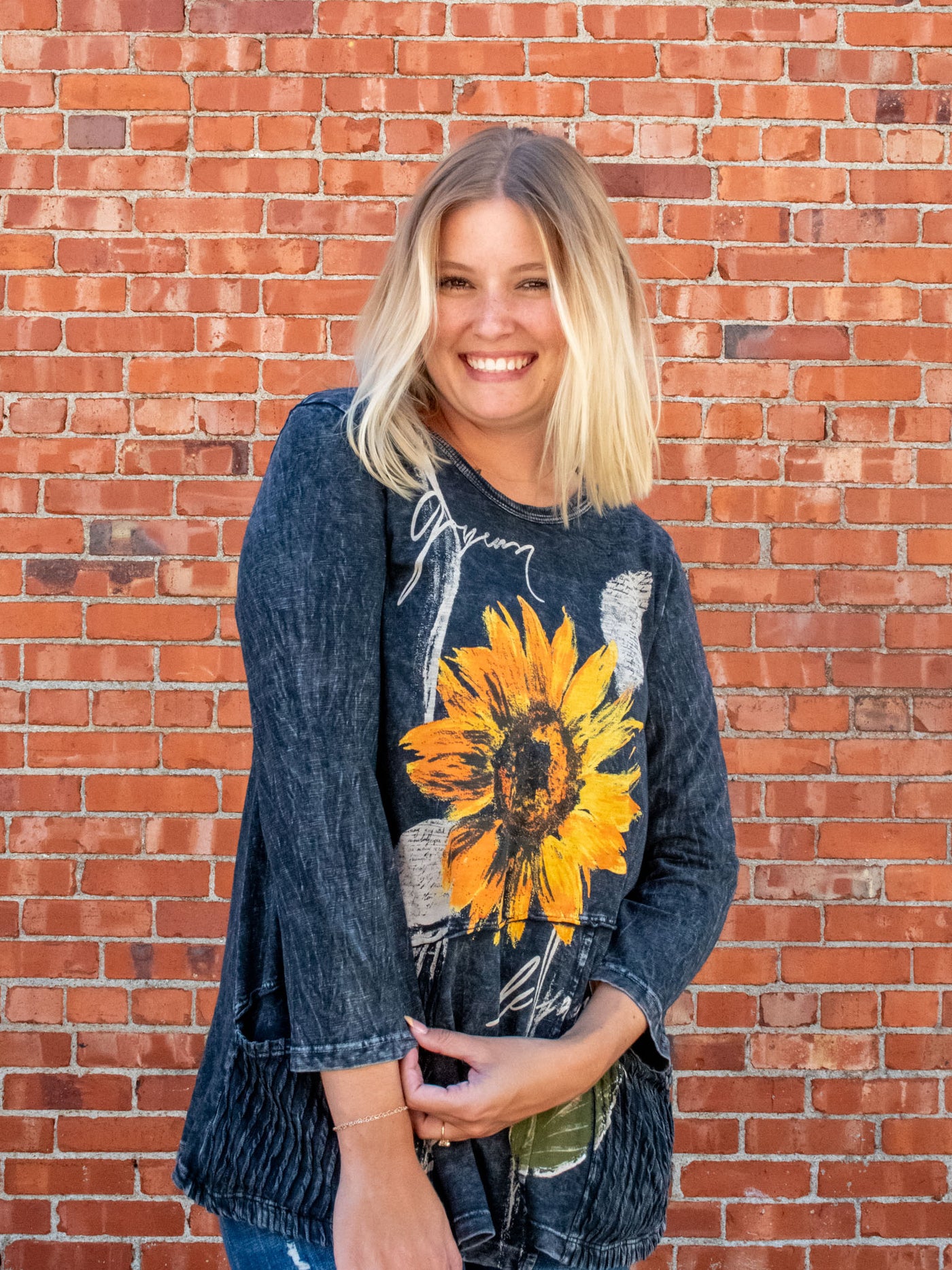 A model wearing a gray, mineral washed, 3/4 sleeve length top with a sunflower graphic. 