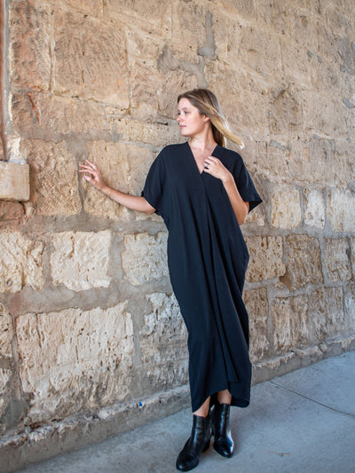 A model wearing a black silk midi kaftan. The model has it paired with black booties.