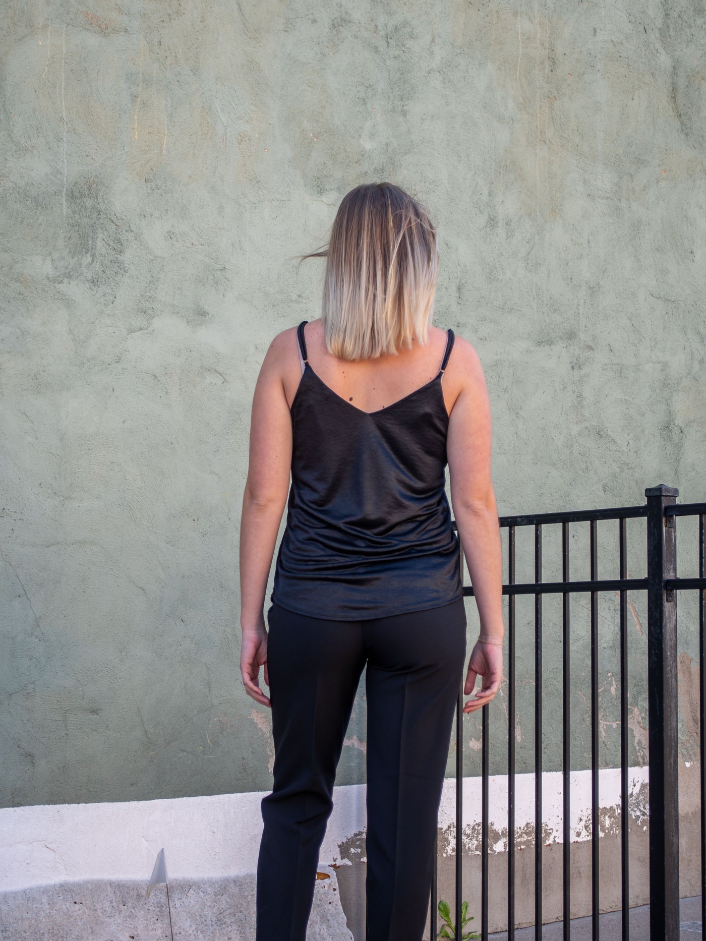 A model wearing a black silk tank with adjustable spaghetti straps. The model is wearing it with black trousers.