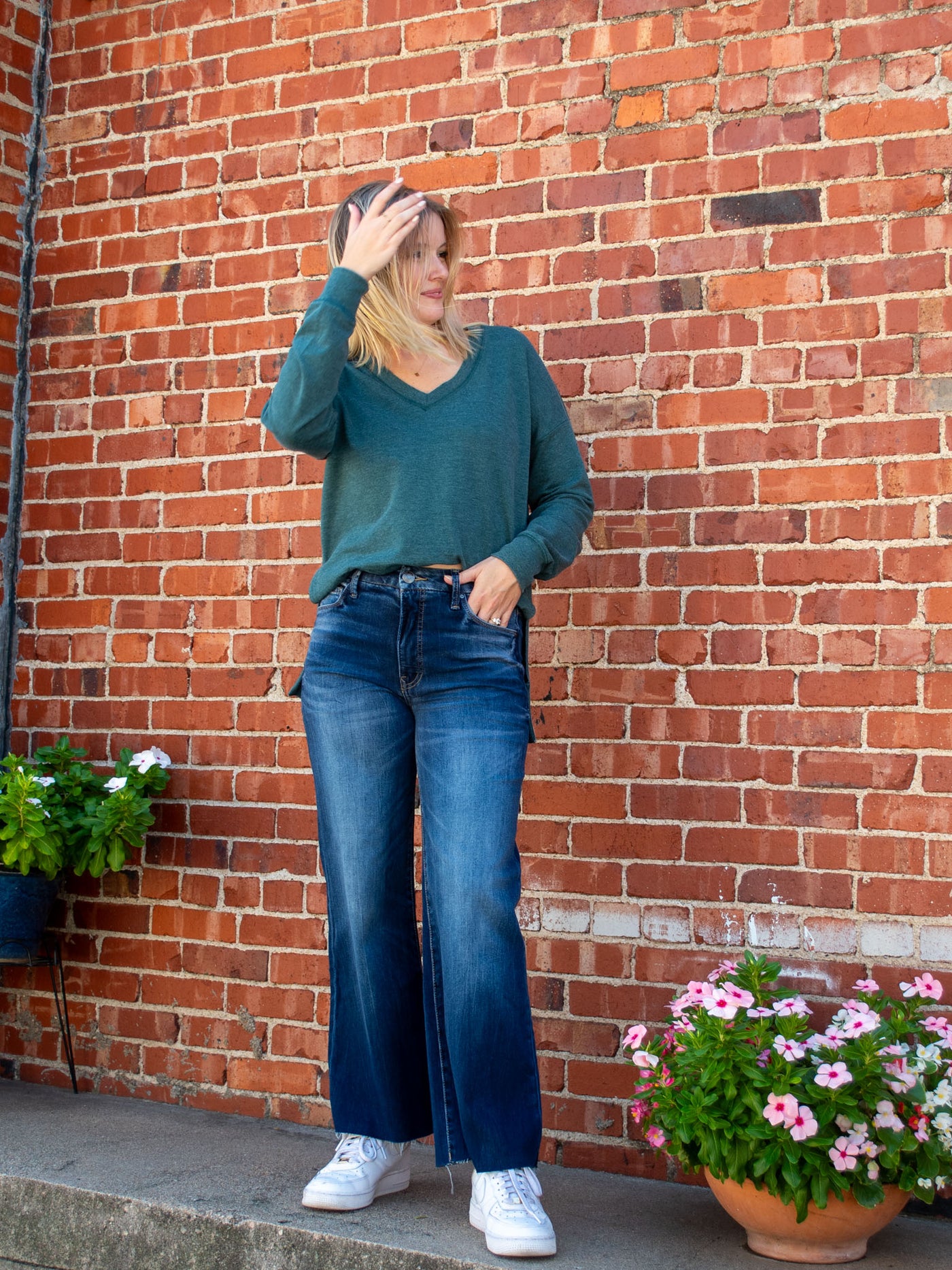 A model wearing a dark wash, faded, wide leg jean with a raw hem. The model has it paired with a teal v-neck top.