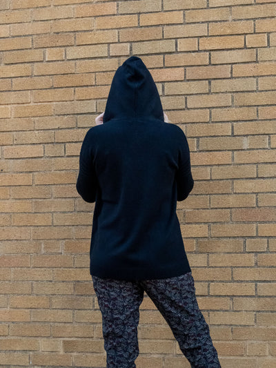 A model wearing a black hooded sweater with drawstrings and pockets. The model has it paired with a black, gray, and red printed jogger.