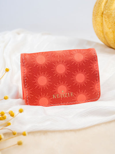 A white card and cash holder with a salmon color and light pink sun pattern on it. The wallet folds and has a gold snap and 3 pockets inside. 