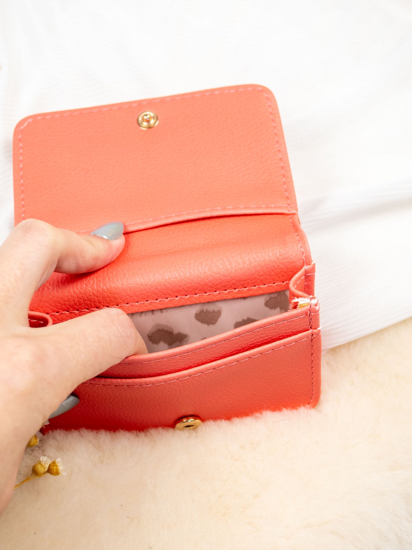 A white card and cash holder with a salmon color and light pink sun pattern on it. The wallet folds and has a gold snap and 3 pockets inside. 