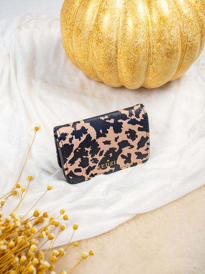 A white card and cash holder with a brown and black leopard print. The wallet folds and has a gold snap and 3 pockets inside. 
