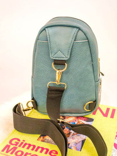 A teal blue vegan leather sling bag with two zipper pockets and a black strap.