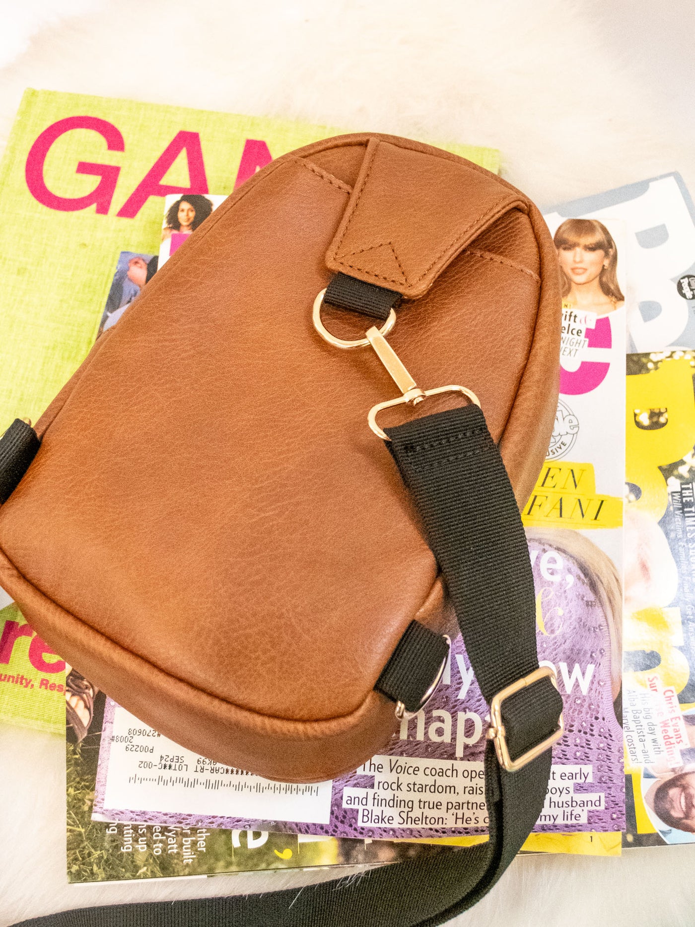 A brown vegan leather sling bag with two zipper pockets and a black strap.