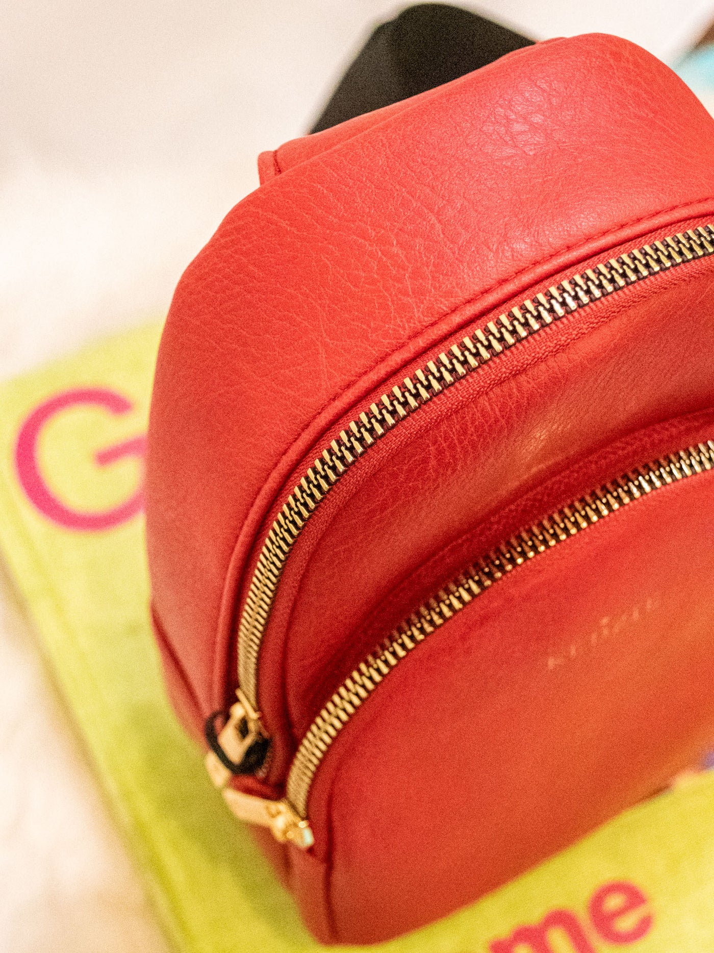 A red vegan leather sling bag with two zipper pockets and a black strap.