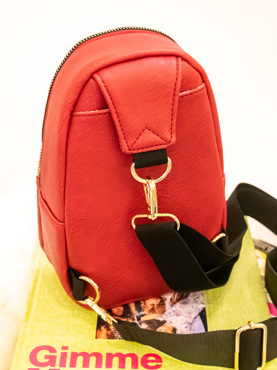 A red vegan leather sling bag with two zipper pockets and a black strap.