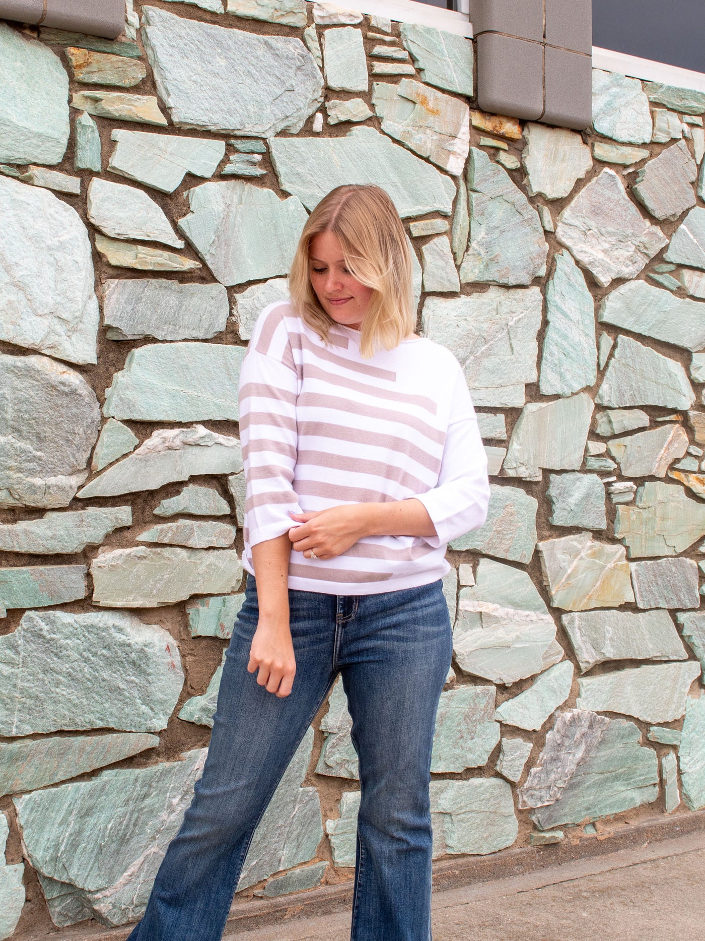 A model wearing a white 3/4 sleeve top with khaki stripes. The model paired it with a pair of dark wash pair of jeans.