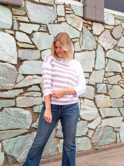 A model wearing a white 3/4 sleeve top with khaki stripes. The model paired it with a pair of dark wash pair of jeans.
