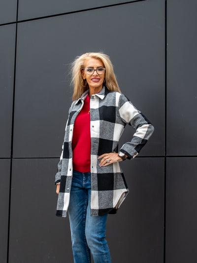 A model wearing a black and white buffalo check long shacket. The model has it paired over a red top and a medium wash jean.