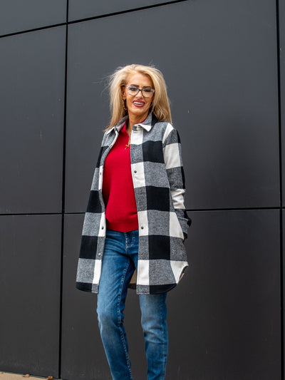 A model wearing a black and white buffalo check long shacket. The model has it paired over a red top and a medium wash jean.