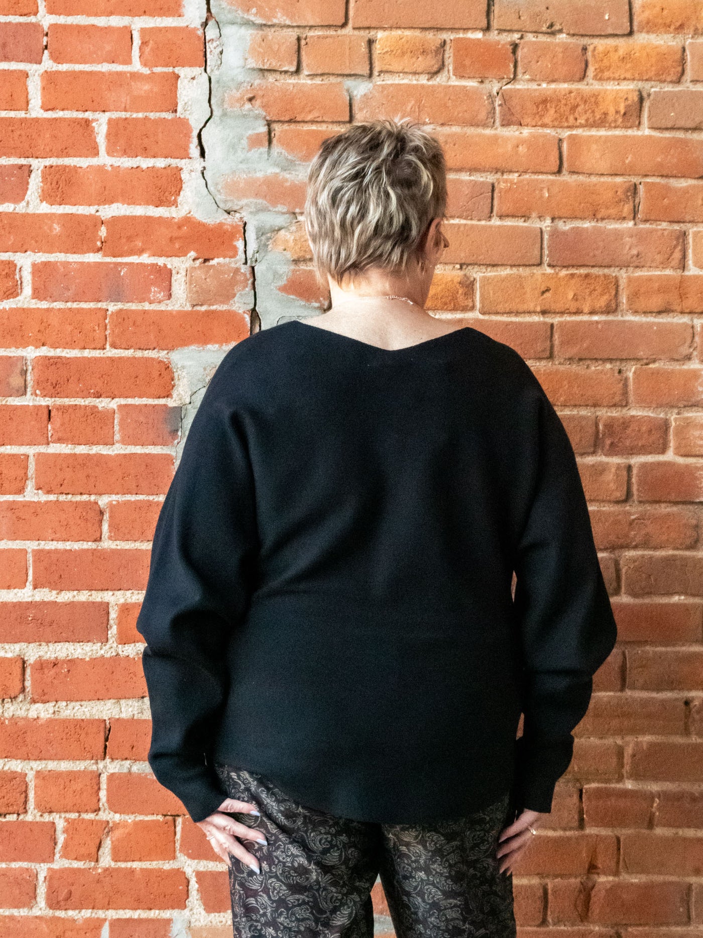 A model wearing a black v-neck knit pullover. The model has it paired with a printed jogger.