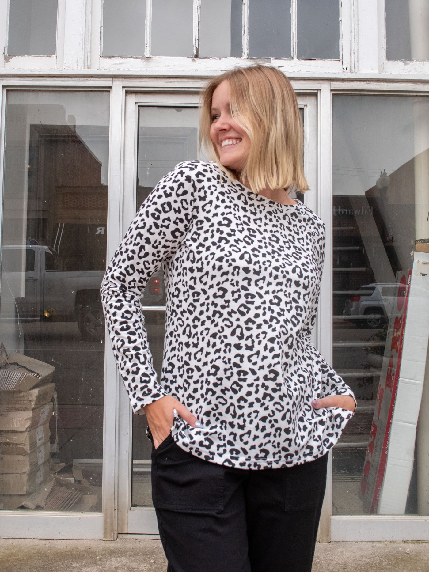 A model wearing a white long sleeve shirt with a black leopard print on it. The model is wearing it with a pair of black drawstring joggers.