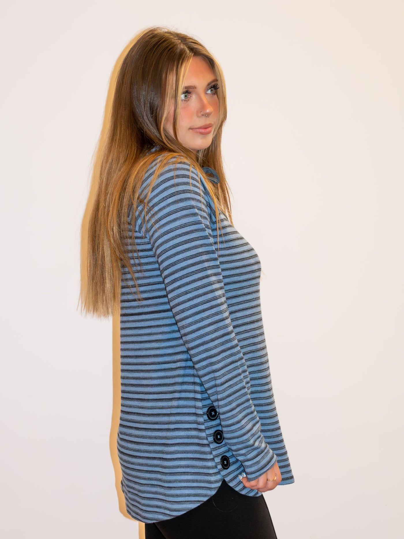 A model wearing a blue and gray striped top with button details on the side. The model has it paired with black leggings.