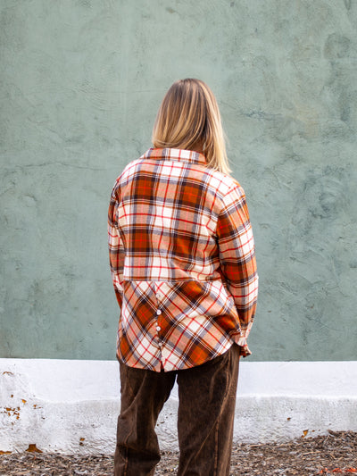 A model wearing a brown plaid button up shirt. The model has it paired with a brown pant and white top.