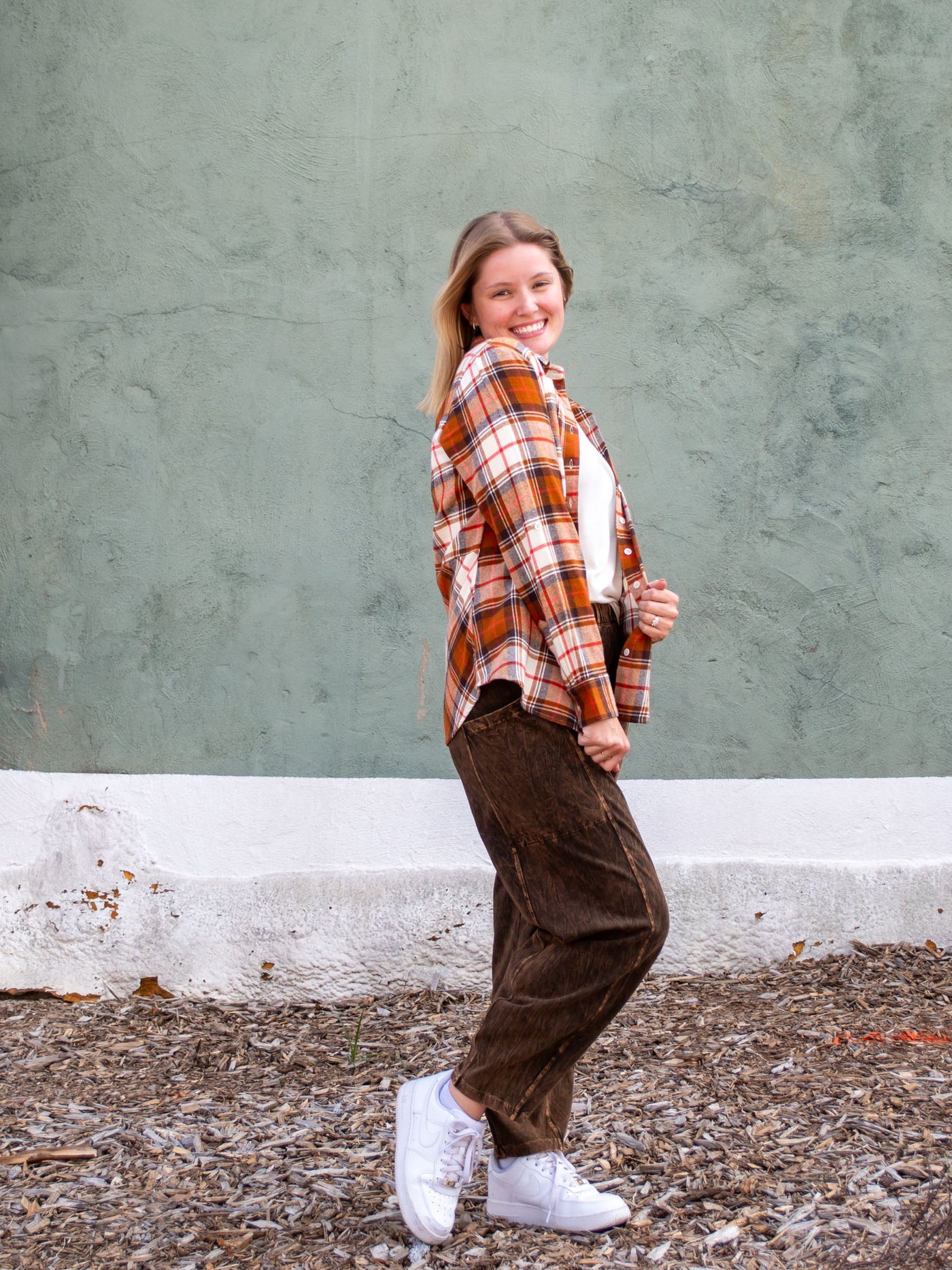 A model wearing a brown plaid button up shirt. The model has it paired with a brown pant, white top, and white sneakers.