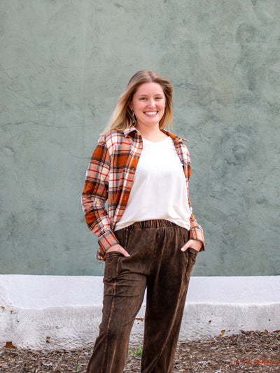 A model wearing a brown plaid button up shirt. The model has it paired with a brown pant and white top.