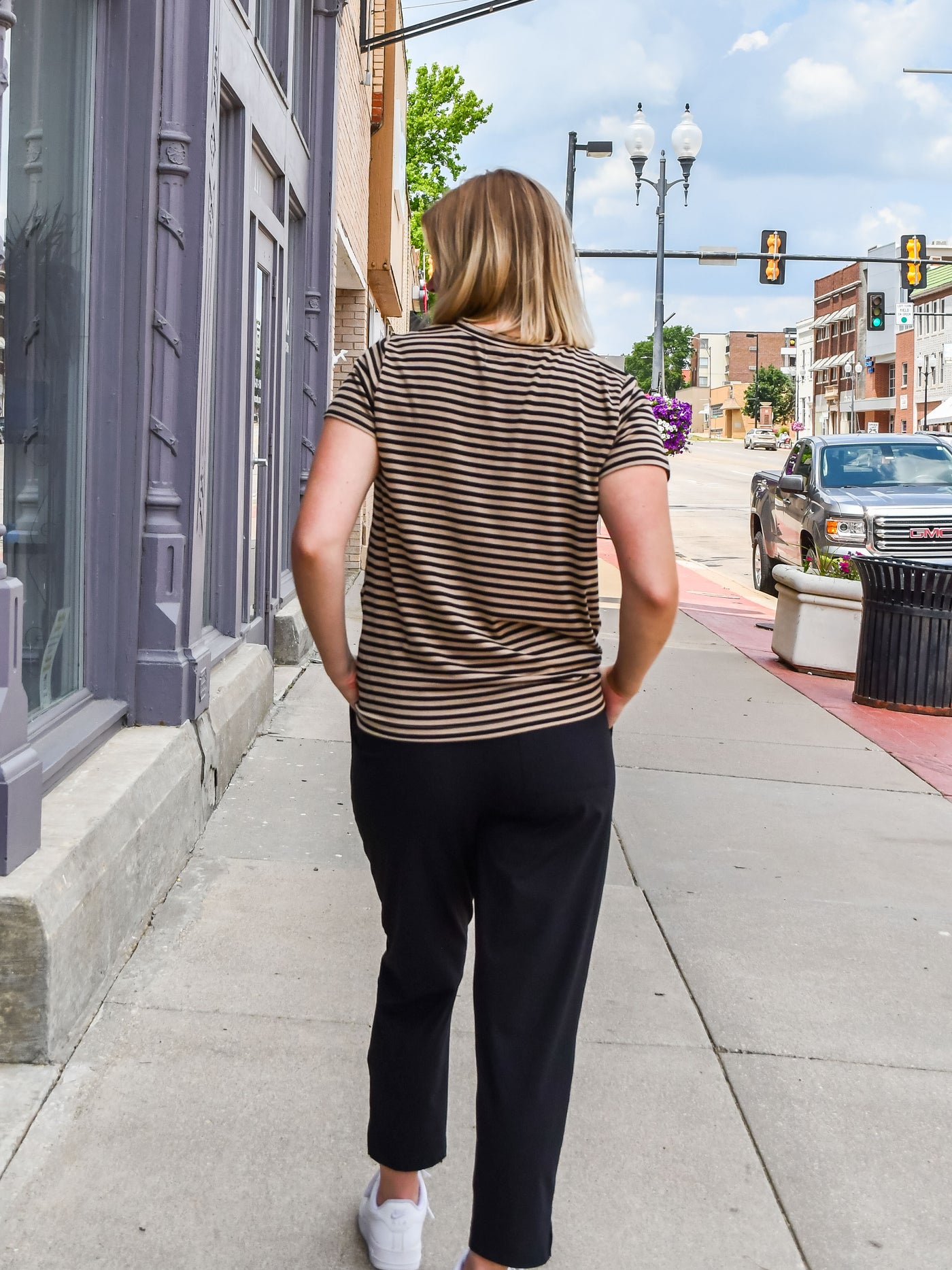 A model wearing a brown striped tee with with a twist front detail. She has it on with slacks. 