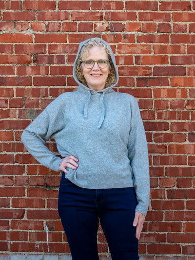 A model wearing a gray knit hooded sweater. The model has it paired with a dark wash skinny jean.