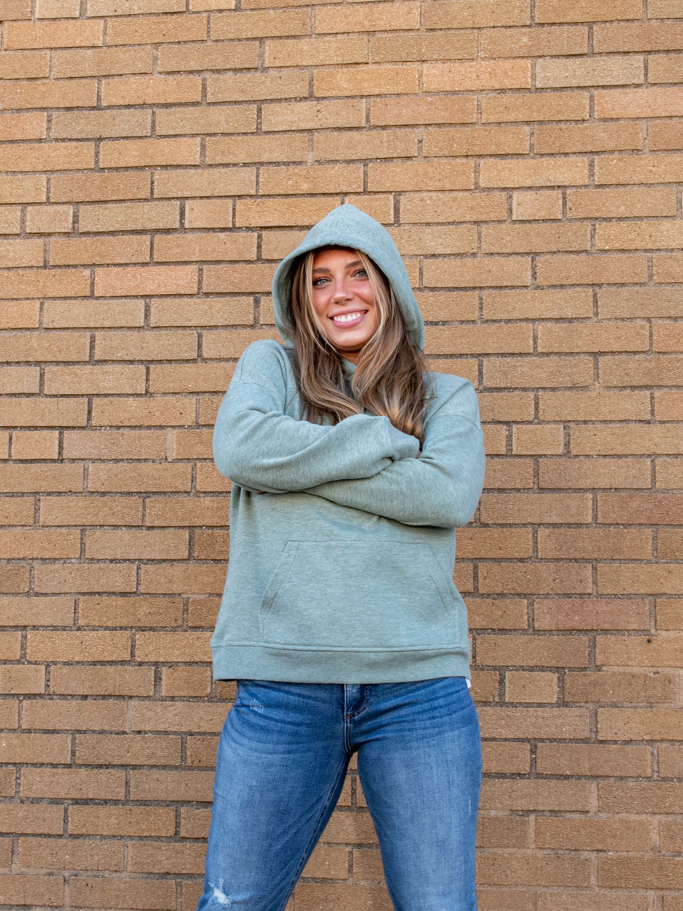 A model wearing a sage green fleece hoodie. The model has it paired with a pair of medium wash jeans.