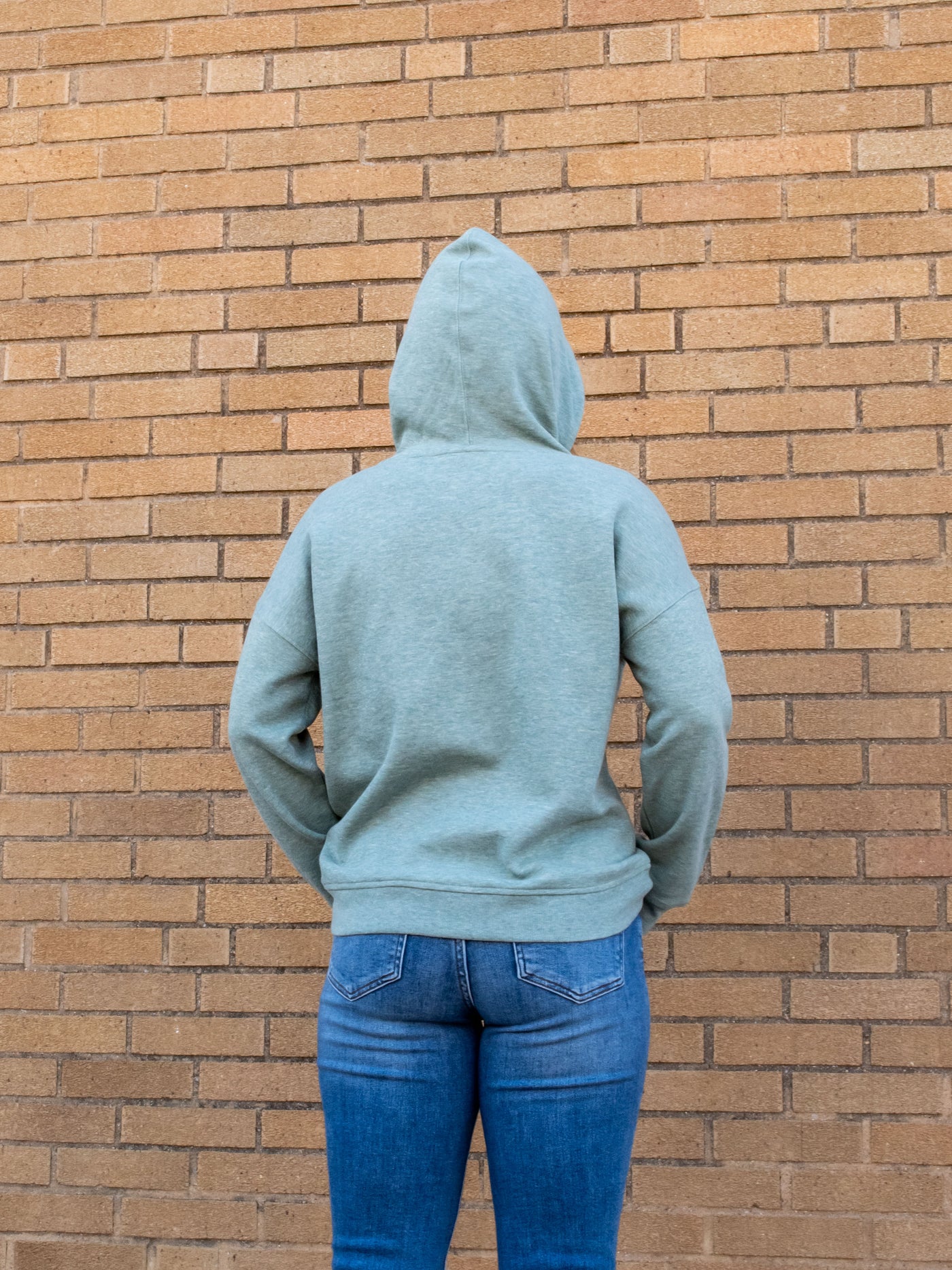 A model wearing a sage green fleece hoodie. The model has it paired with a pair of medium wash jeans.