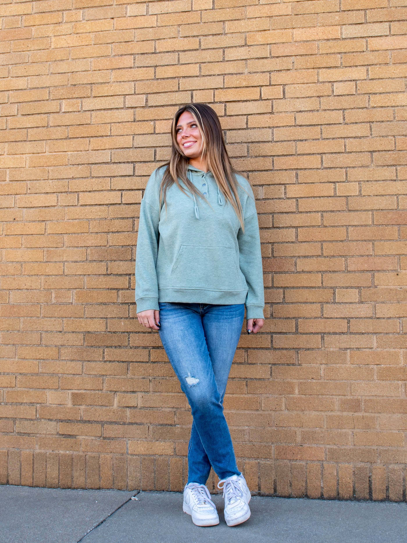 A model wearing a sage green fleece hoodie. The model has it paired with a pair of medium wash jean and white sneakers.