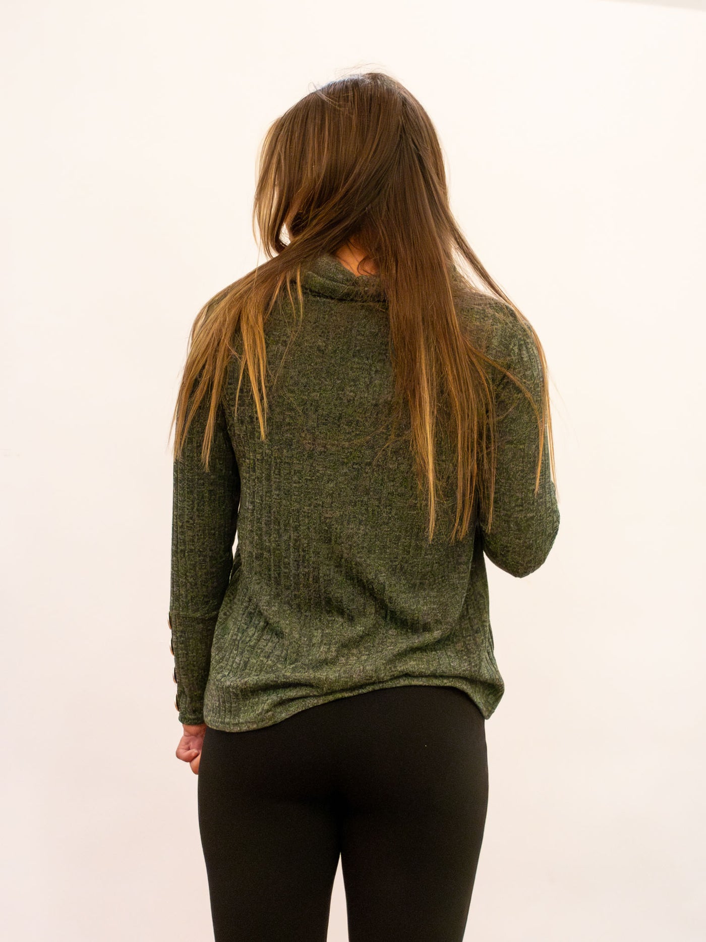 A model wearing an olive green sweater with a cowl neck detail. The model has it paired with black leggings.
