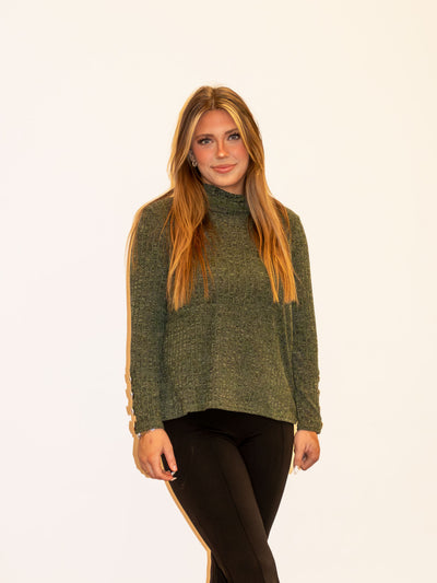 A model wearing an olive green sweater with a cowl neck detail. The model has it paired with black leggings.