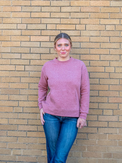 A model wearing a red crewneck sweatshirt with a front pocket and side slits. The model has it paired with a dark wash jean.