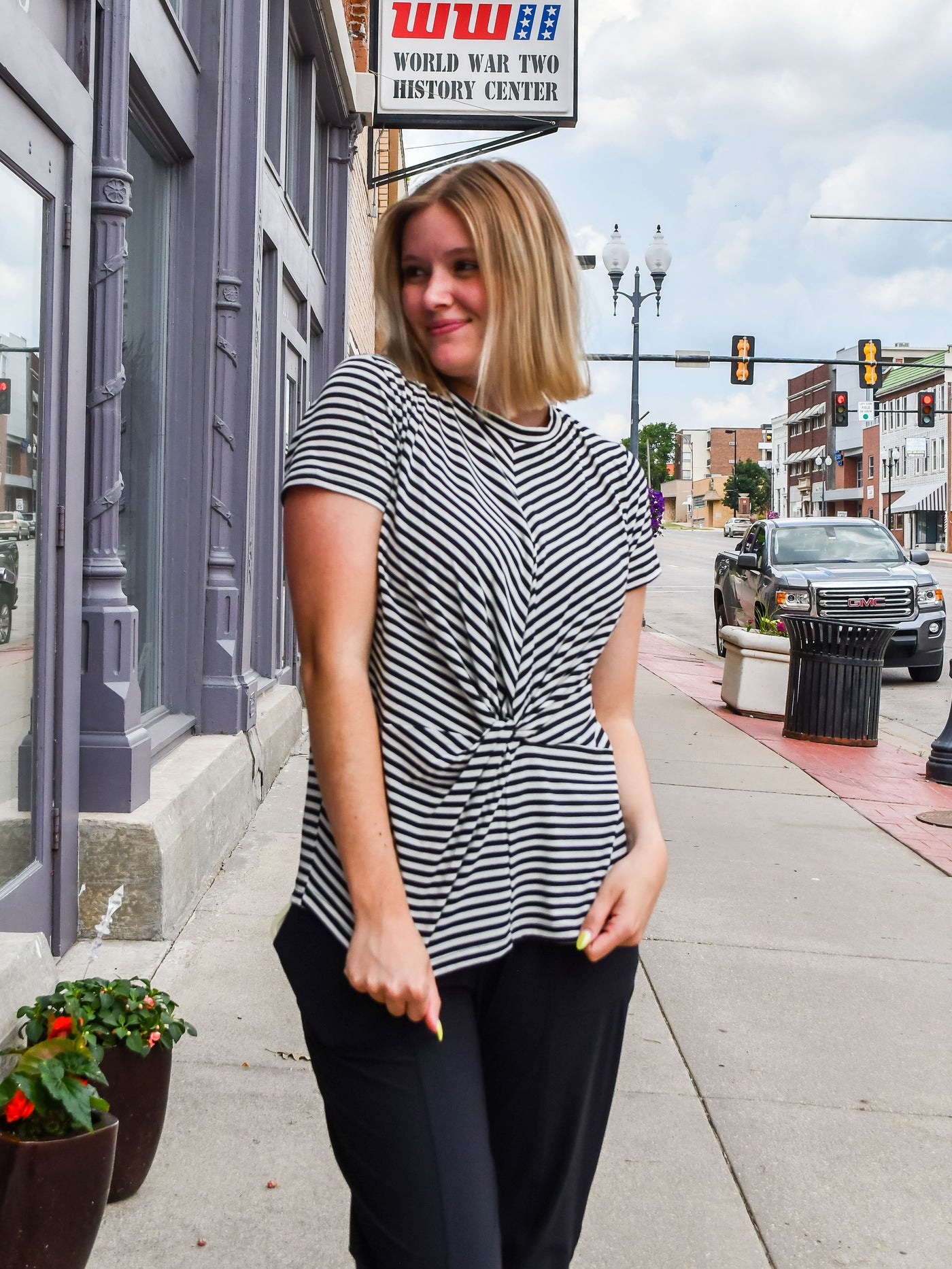 A model wearing a black striped tee with with a twist front detail. She has it on with slacks. 