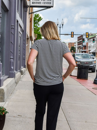A model wearing a black striped tee with with a twist front detail. She has it on with slacks. 