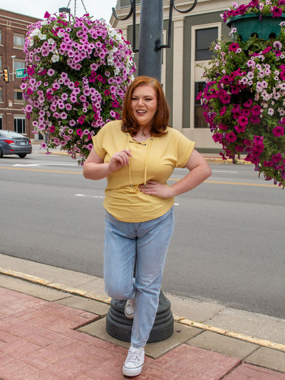 A model wearing a yellow striped top with a lace up neckline detail. The model paired it with a pair of light wash skinny jeans and white sneakers.