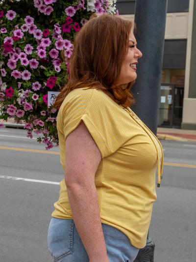 A model wearing a yellow striped top with a lace up neckline detail. The model paired it with a pair of light wash skinny jeans and white sneakers.