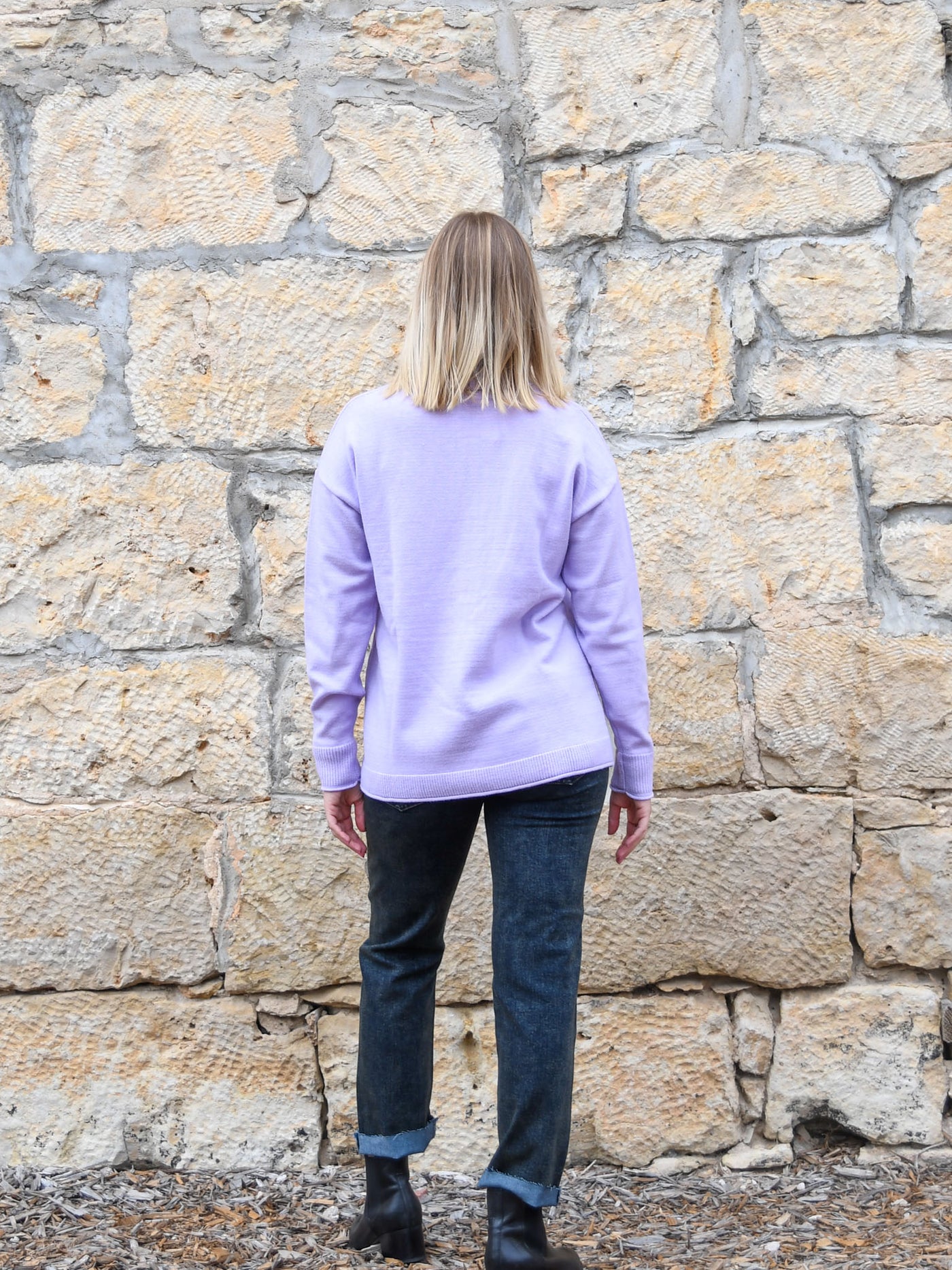 A model wearing a lavender colored turtleneck sweater. The model has it paired with a gray acid wash jean and black booties.