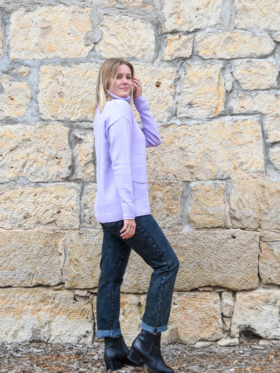 A model wearing a lavender colored turtleneck sweater. The model has it paired with a gray acid wash jean and black booties.