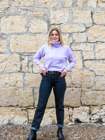 A model wearing a gray acid wash, straight leg jean. The model has it paired with a lavender colored sweater and black booties.