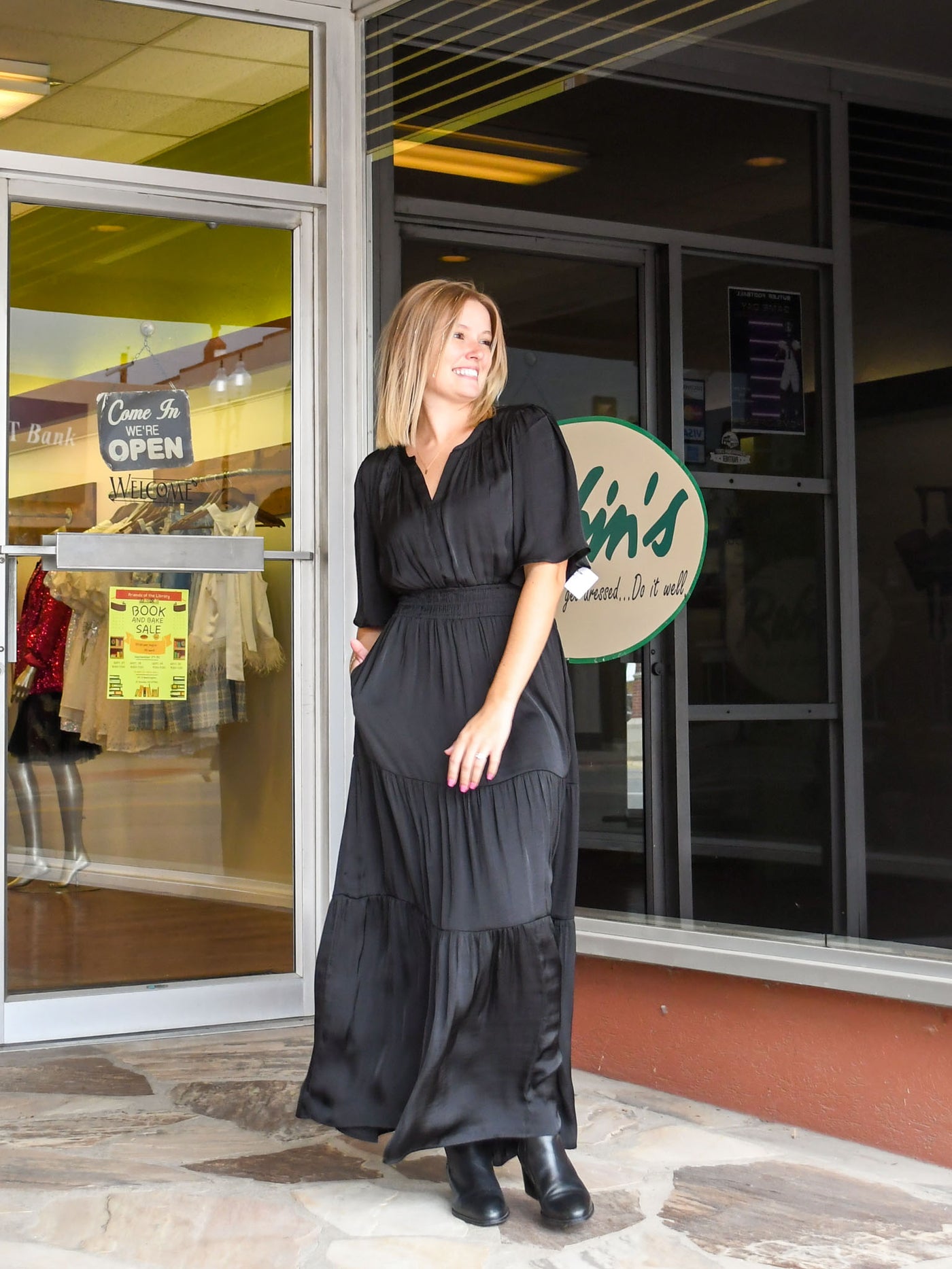 A model wearing a black tiered maxi dress with a long, short sleeve. The model has it paired with a black bootie.