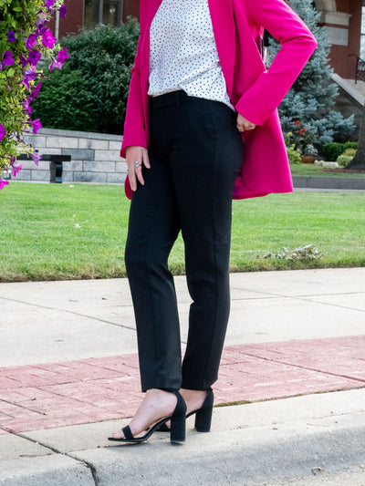 A model wearing a black ankle length trouser. The model has it paired with a white polkadot blouse, a pink blazer and black heels.
