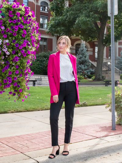 A model wearing a black ankle length trouser. The model has it paired with a white polkadot blouse, a pink blazer and black heels.