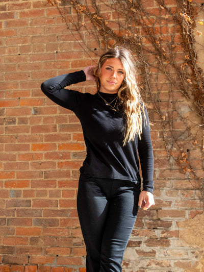 A model wearing a black mock neck sweater with a white seam detail down the sleeve. The model has it paired with black jeans.