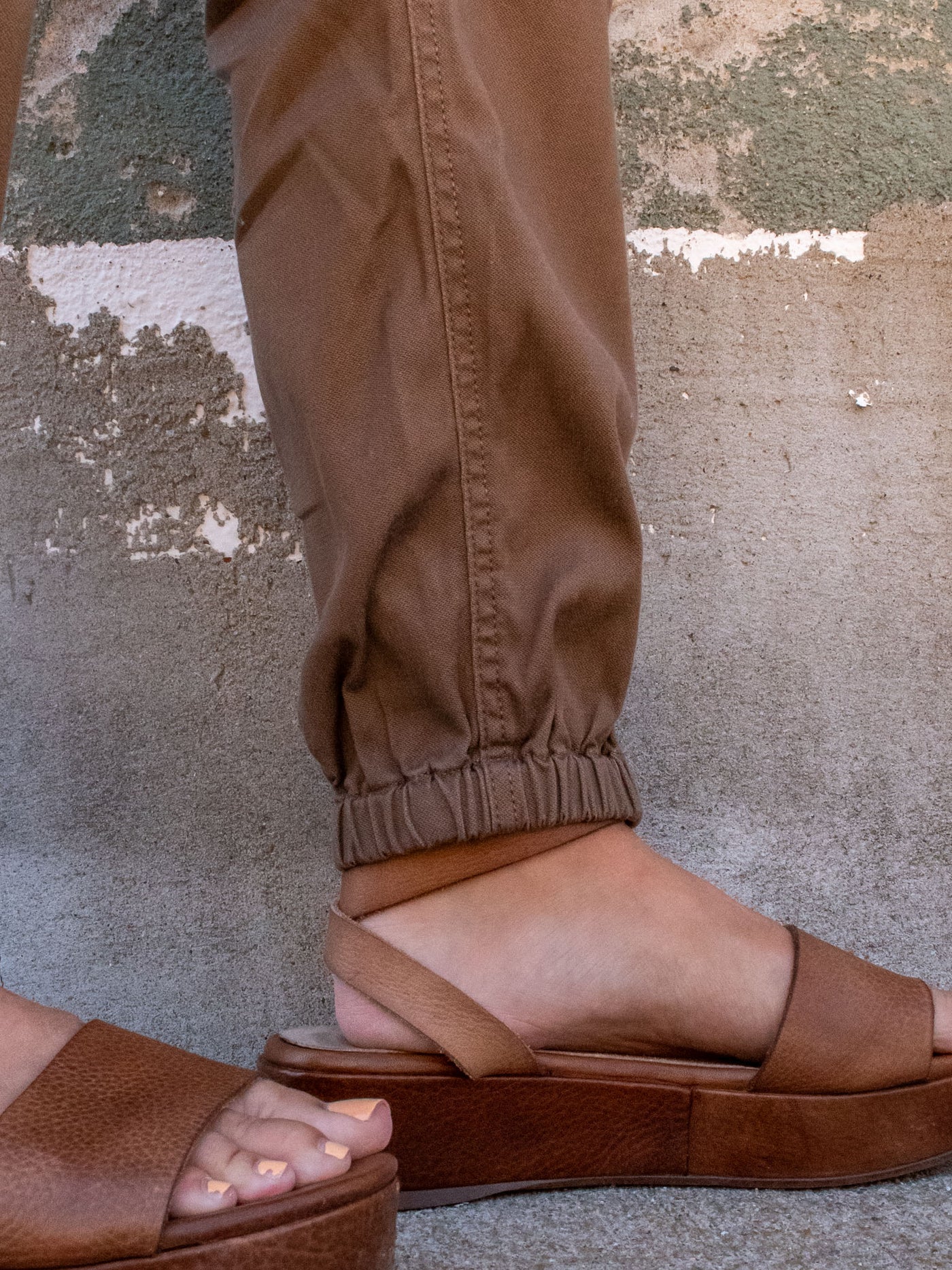 A model wearing a pair of brown cropped utility pants with a zipper hem. The model has them paired with brown platform sandals.