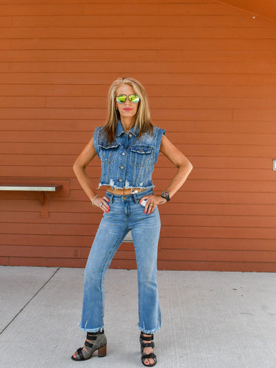 A model wearing a pair of mid-rise crop flare jeans with a denim vest buttons up and heels.