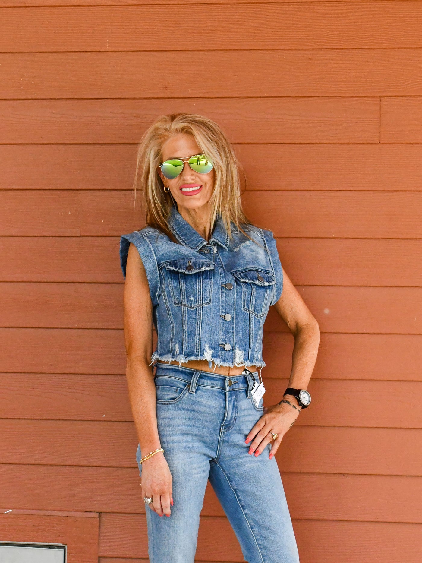 A model wearing a distressed vintage cropped denim vest buttoned up. She has it paired with crop flare fray hem jeans and booties. 