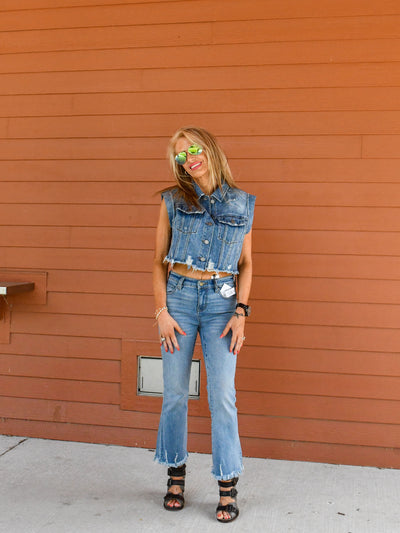 A model wearing a distressed vintage cropped denim vest buttoned up. She has it paired with crop flare fray hem jeans and booties. 