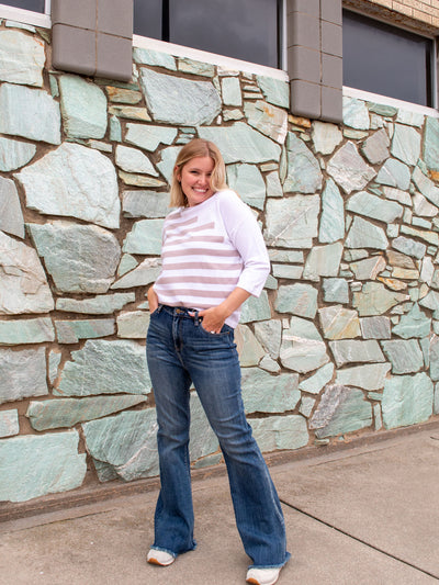 A model wearing a pair of dark wash, flare jeans. The model is wearing it with a white and khaki striped top and sneakers.