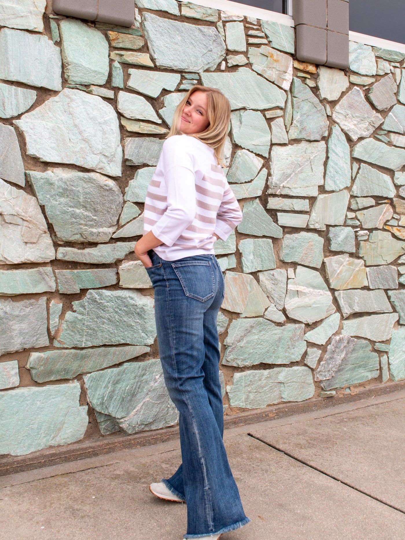 A model wearing a pair of dark wash, flare jeans. The model is wearing it with a white and khaki striped top.