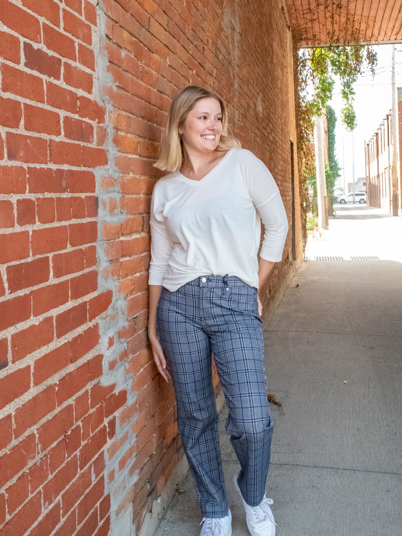 A model wearing a pair of navy, plaid, slim dress pants. She has them paired with a white top and white sneakers.