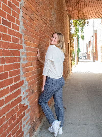 A model wearing a pair of navy, plaid, slim dress pants. She has them paired with a white top and white sneakers.